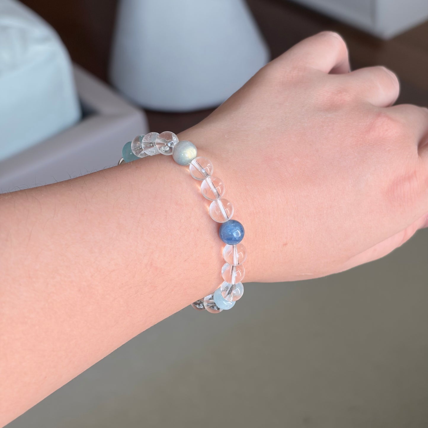 Blue Kyanite Grey Moonstone Alpine Dawn Bracelet worn on the wrist, a Water element bracelet with clear quartz, grey moonstone, and blue kyanite accents in a cool blue-grey palette.