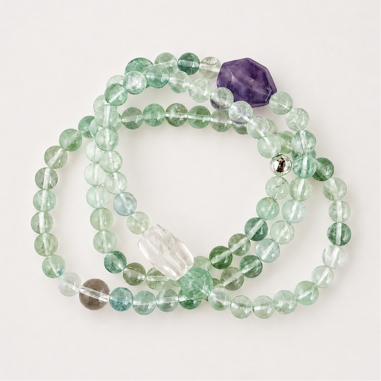 Green fluorite, clear quartz, and amethyst multi-wrap bracelet on a soft light gray background.