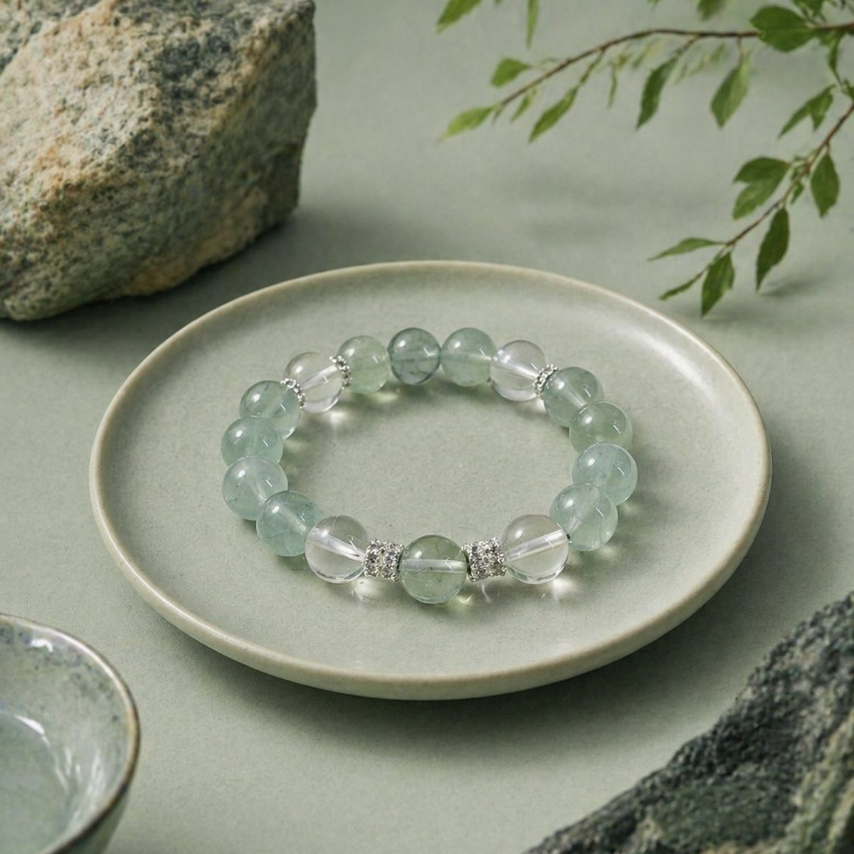 Green fluorite clear quartz bracelet styled on a ceramic plate with natural stone and leaves