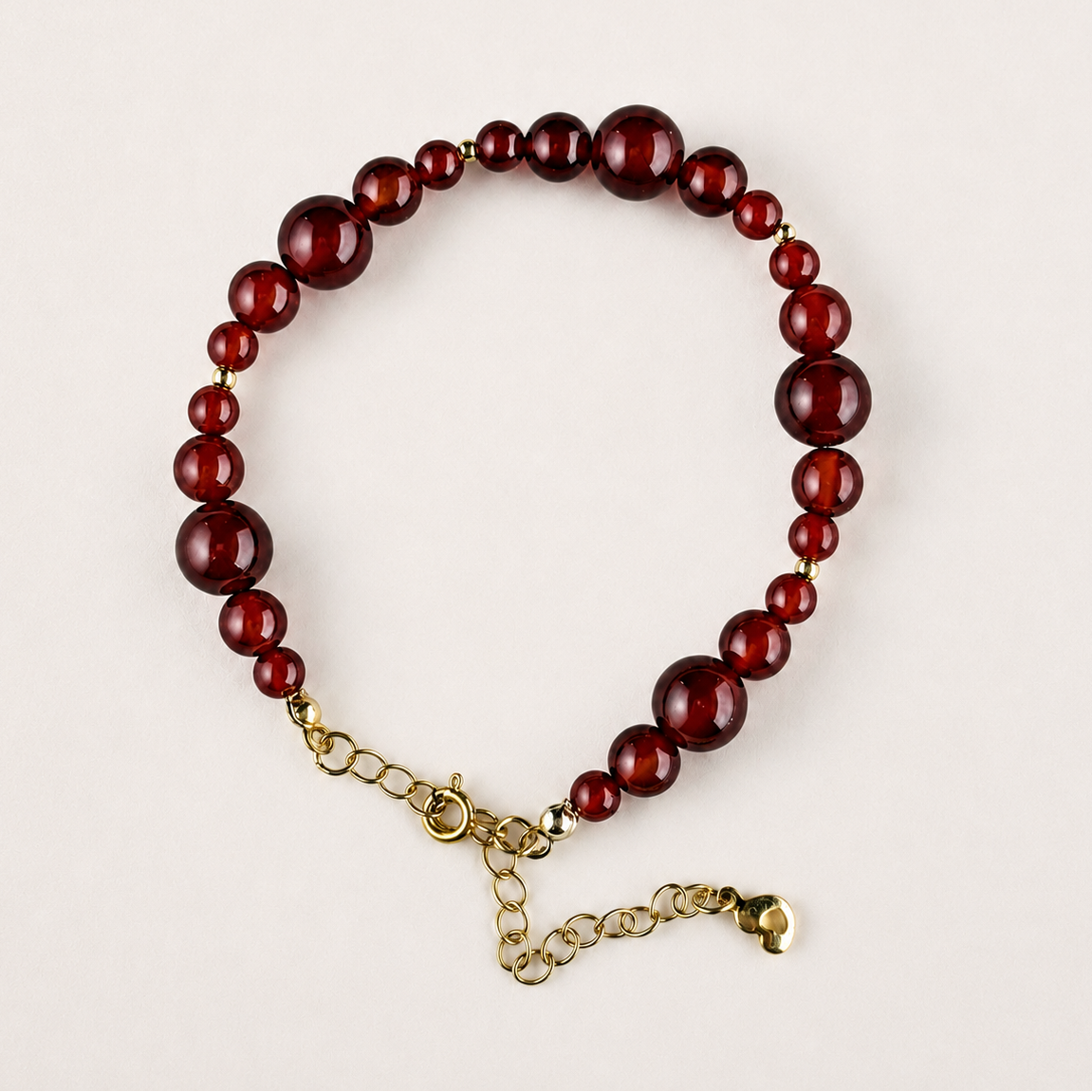 Red agate beaded bracelet with mixed 4–8mm beads, gold-tone spacer beads, and adjustable chain on a light gray background.