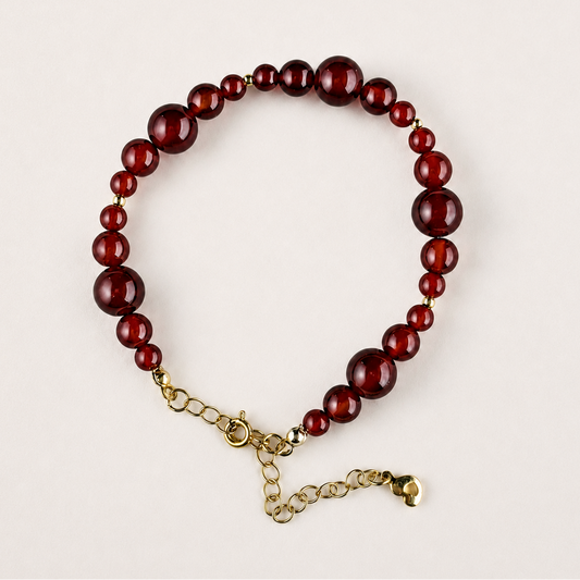 Red agate beaded bracelet with mixed 4–8mm beads, gold-tone spacer beads, and adjustable chain on a light gray background.