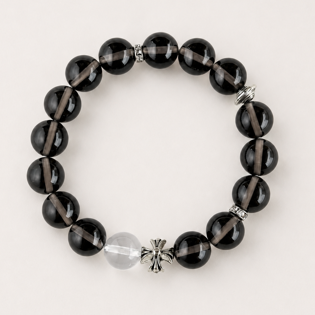 Smoky quartz beaded bracelet with a clear accent bead and silver-toned charm on a warm neutral background.
